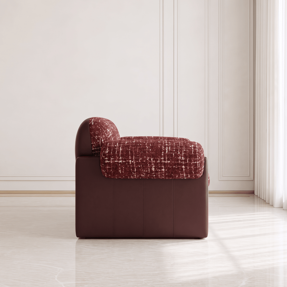 A modern low-profile armchair with a dark brown leather-like base and textured reddish-brown bouclé seat and back cushions, shown in a minimalist cream-colored room with soft window light.
